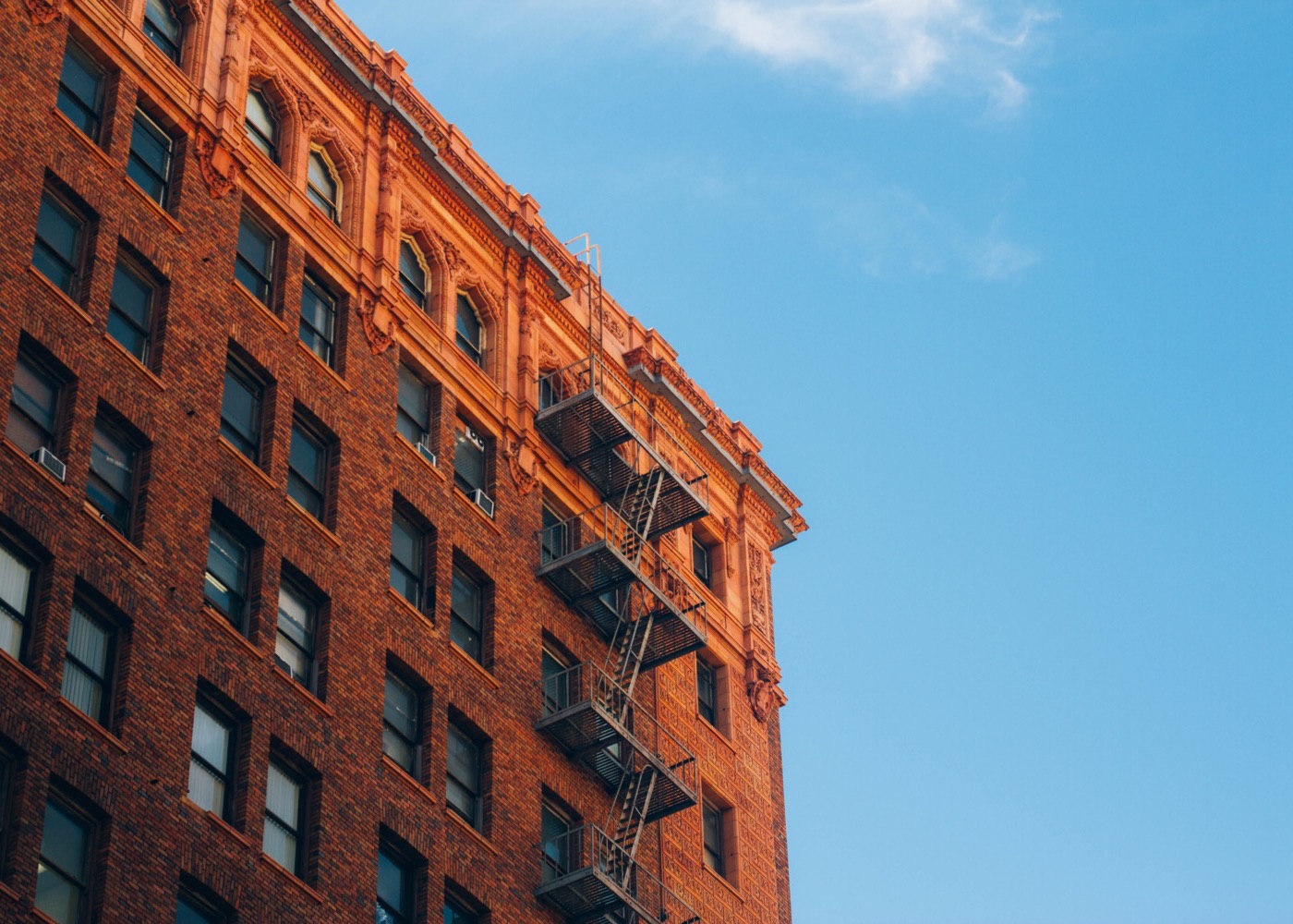 Upper floors of a brick multifamily apartment building with iron fire escapes against a clear blue sky